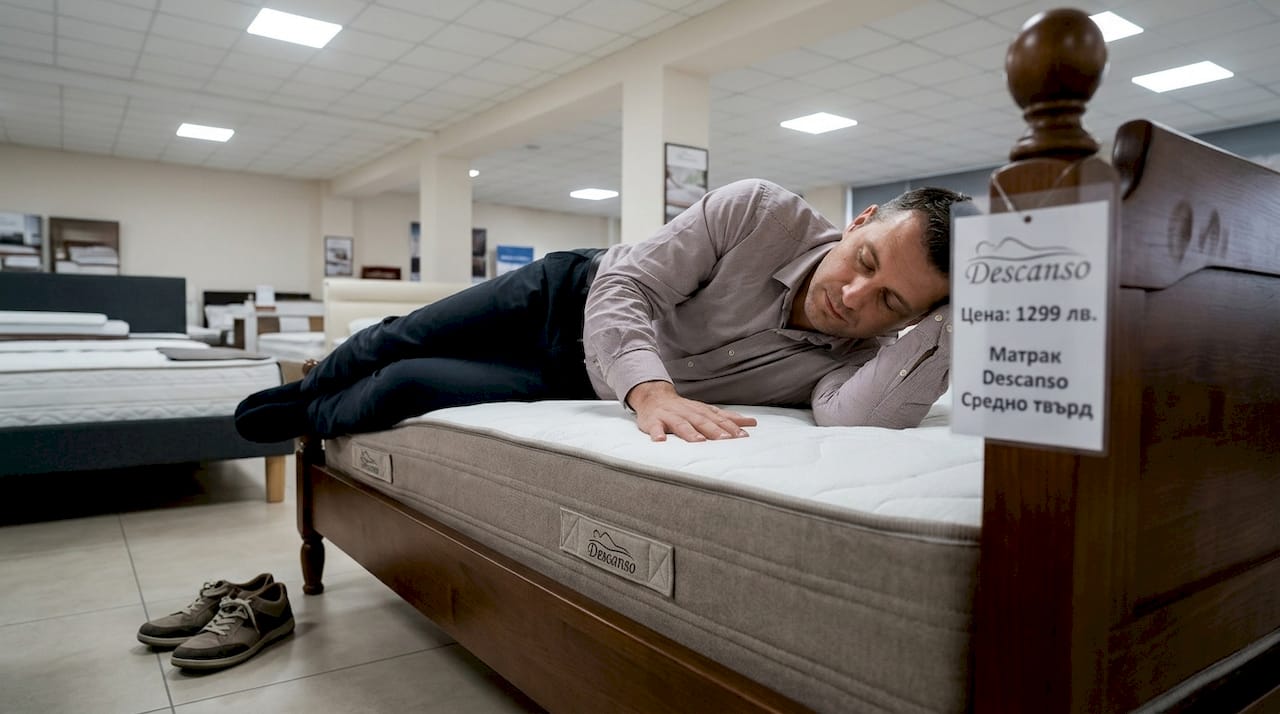 Мъж изпробва различни матраци в магазин за мебели, за да избере най-удобния за себе си.