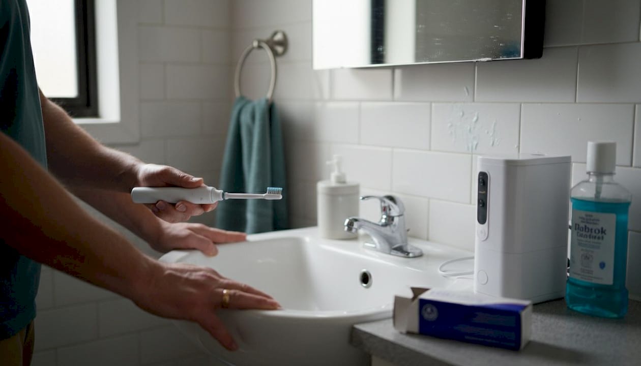 Hands using sonic toothbrush at bathroom sink