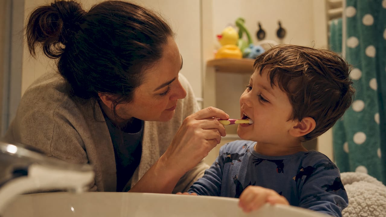 Parent supervising child brushing teeth