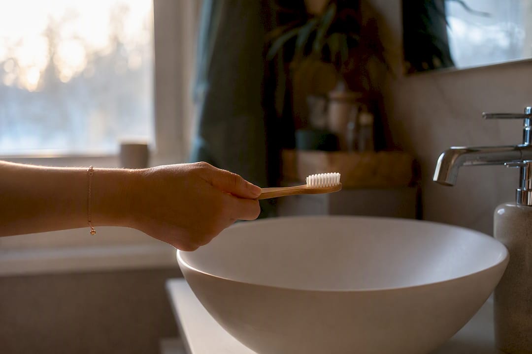Hand holding soft-bristled toothbrush above bathroom sink