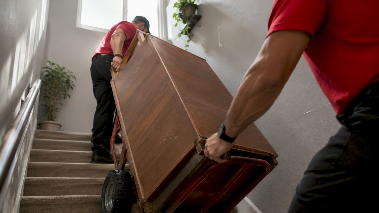 Close-up of movers carrying wooden cabinet on dolly