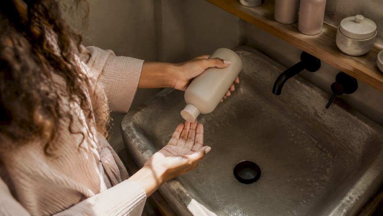 En person trykker fugtgivende shampoo ud i hænderne på badeværelset.