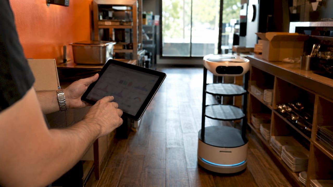 Hands operating AI tools with hospitality robots nearby