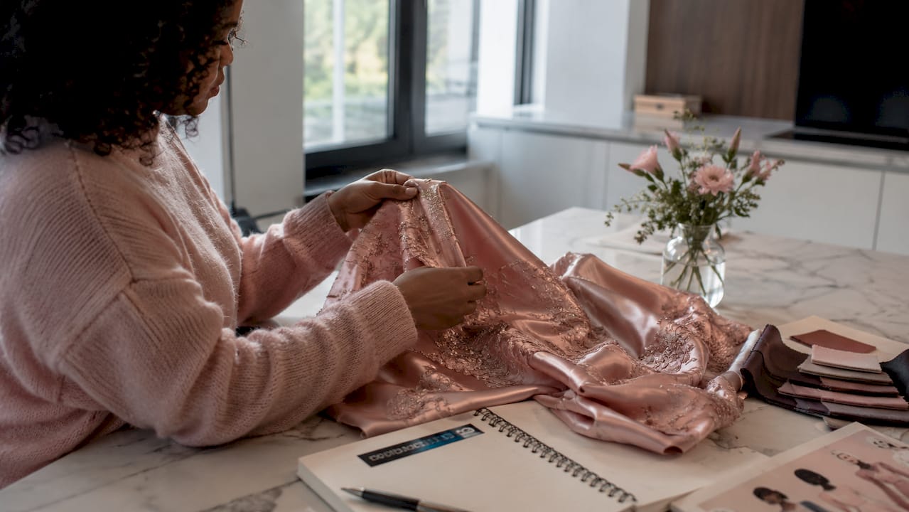 Hands inspecting satin embroidered Bebe fabric sample