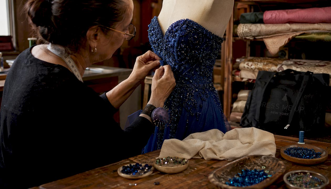 Hands sewing beadwork on gown