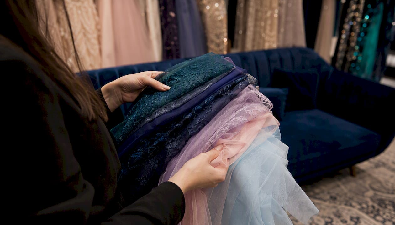 Hands holding gala dress fabric swatches under chandelier light