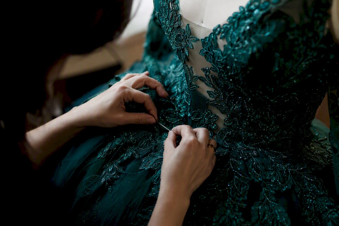 Hands sewing lace on formal gown