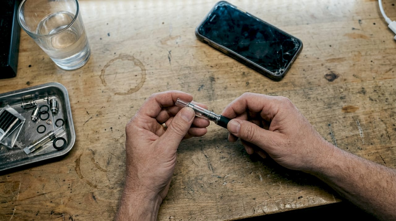 Hands assembling vape pen at well-used workbench