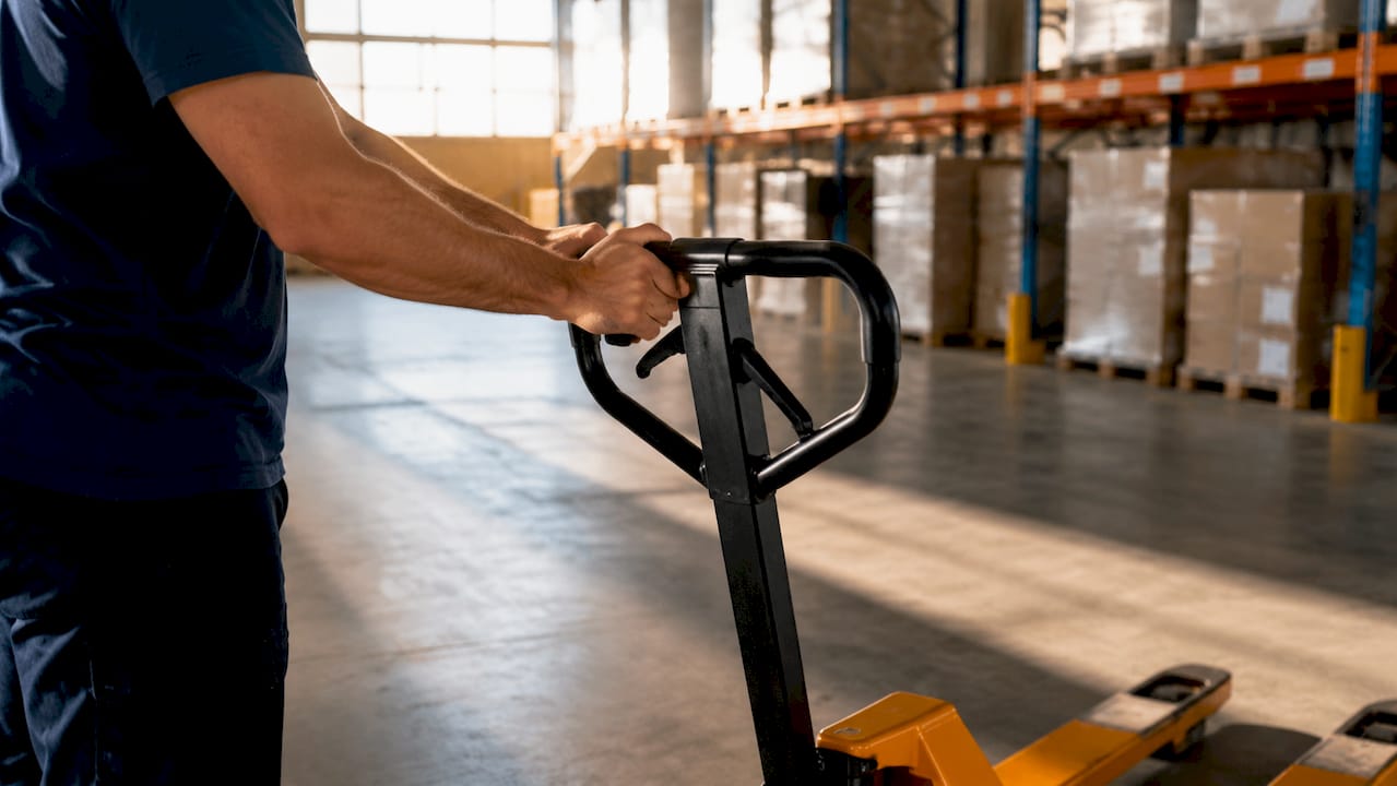 Hands pushing pallet jack in warehouse