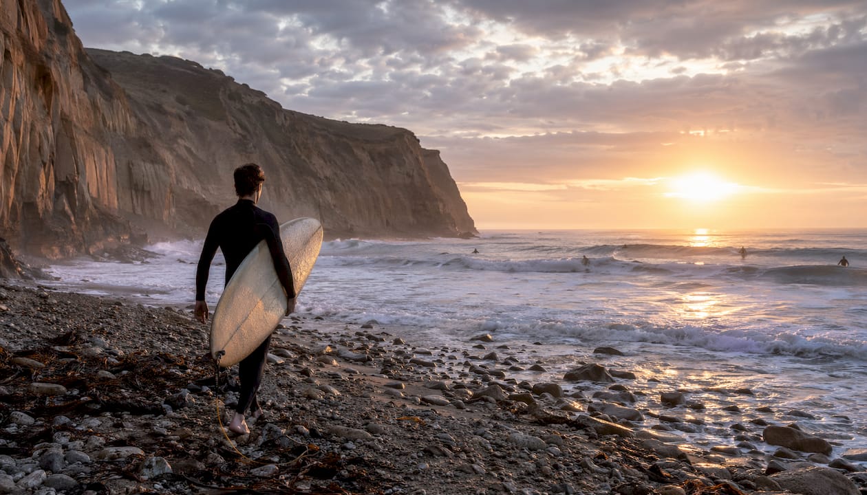 Surfer walking on La Jolla beach at dawn