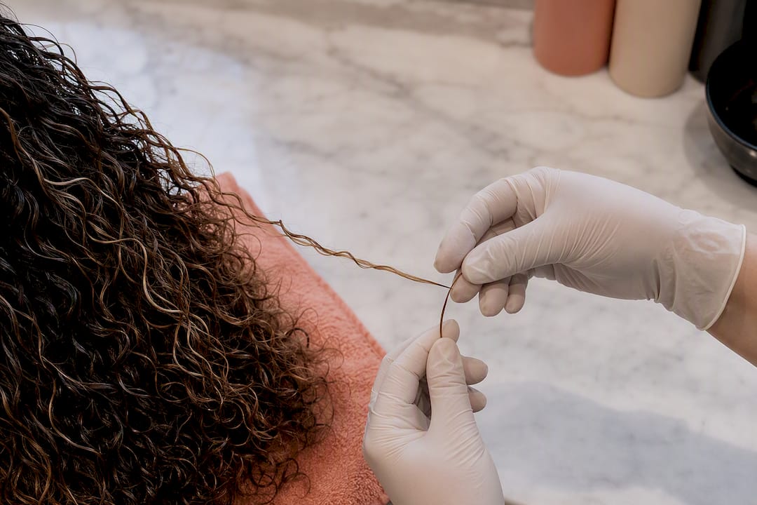 Colorist checking curl elasticity before lightening