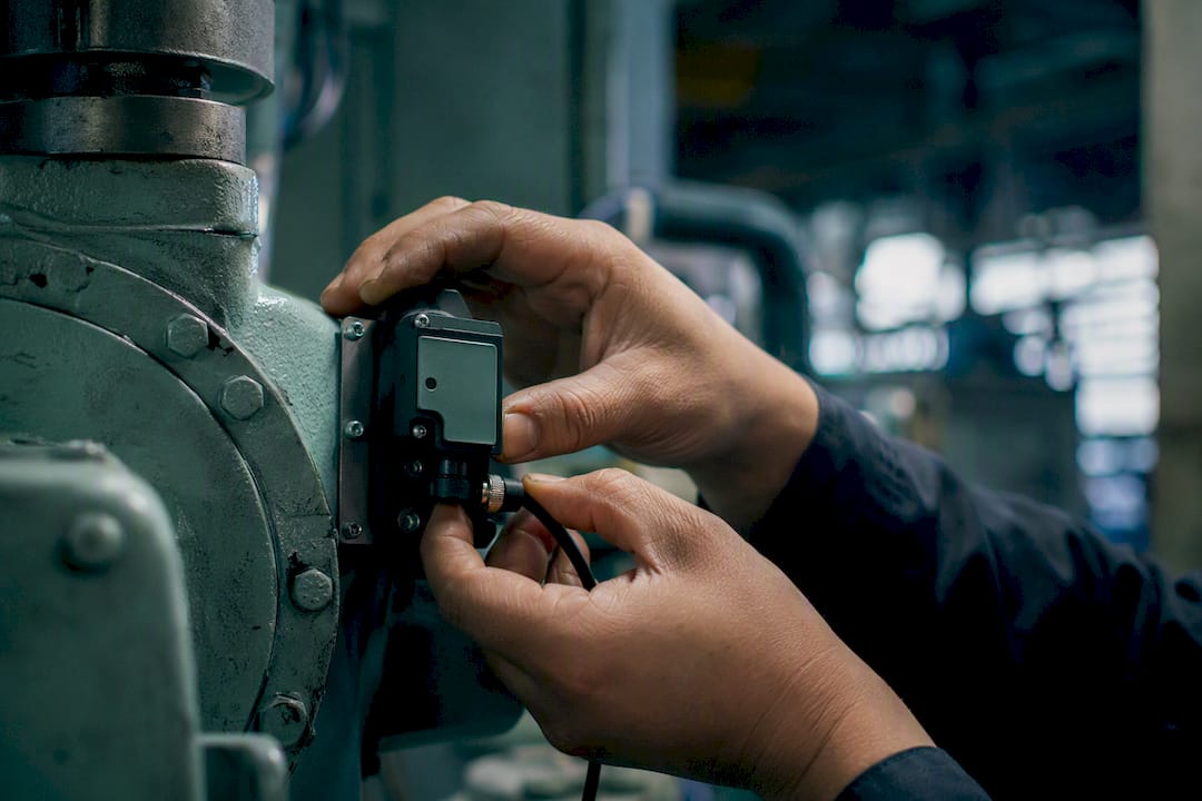 Hands installing automated sensor on factory machine