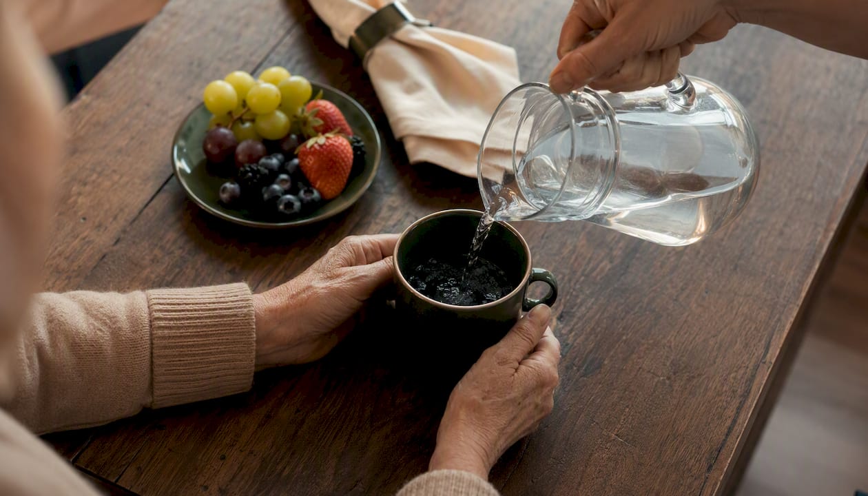 Carer pouring water into glass for elder