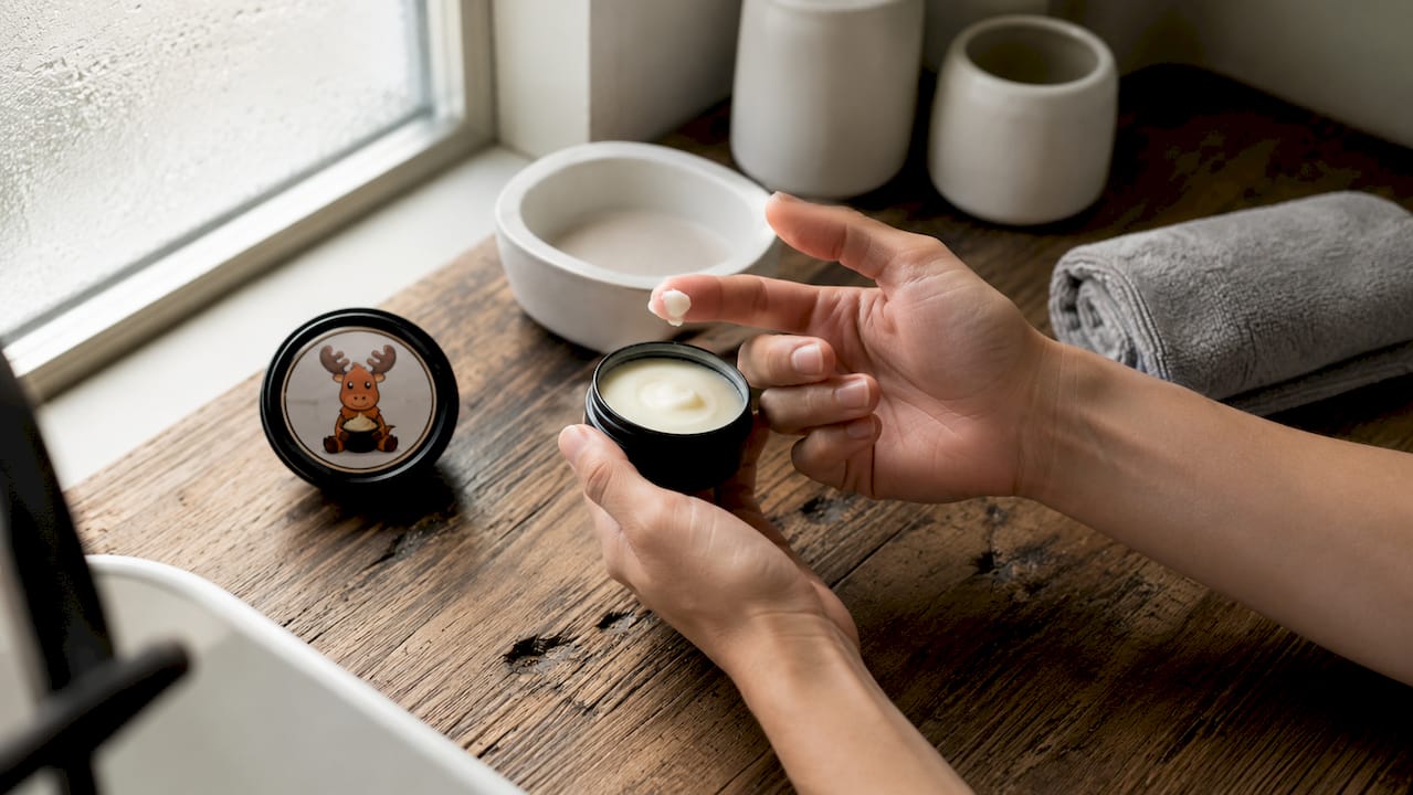 Hands holding open black tin deodorant with balm on fingertip