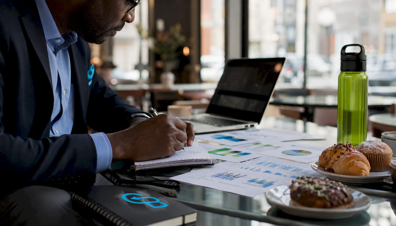Hands typing on laptop beside CRM printouts