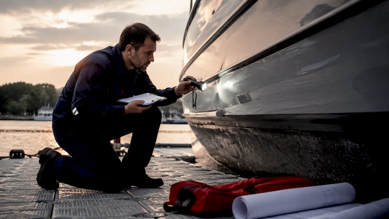 Marine surveyor inspecting yacht hull at dock