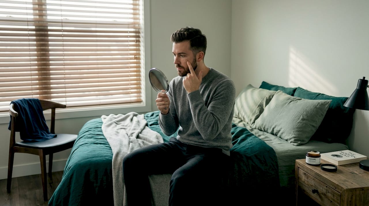 Man blending concealer, checking face for mistakes