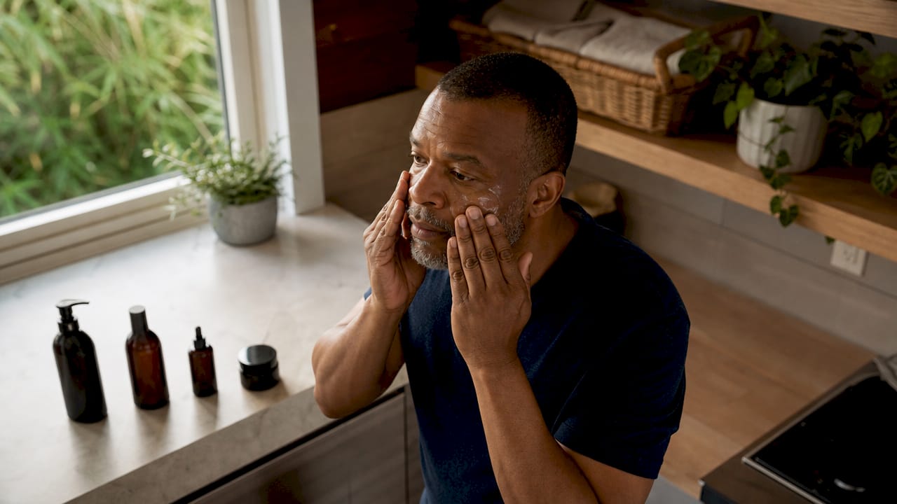 Man applying moisturizer on face at vanity