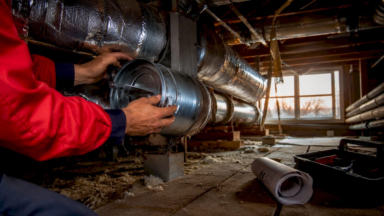 Hands adjusting damper inside home attic ductwork