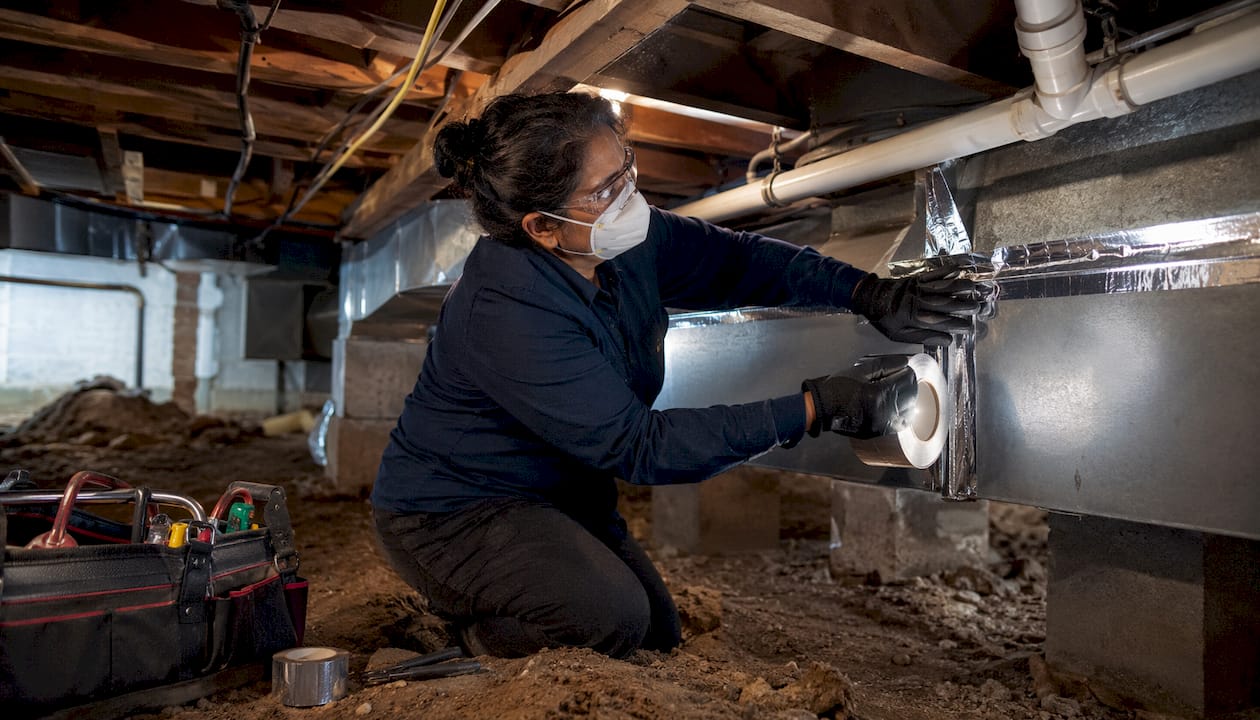Woman sealing air duct seams in attic
