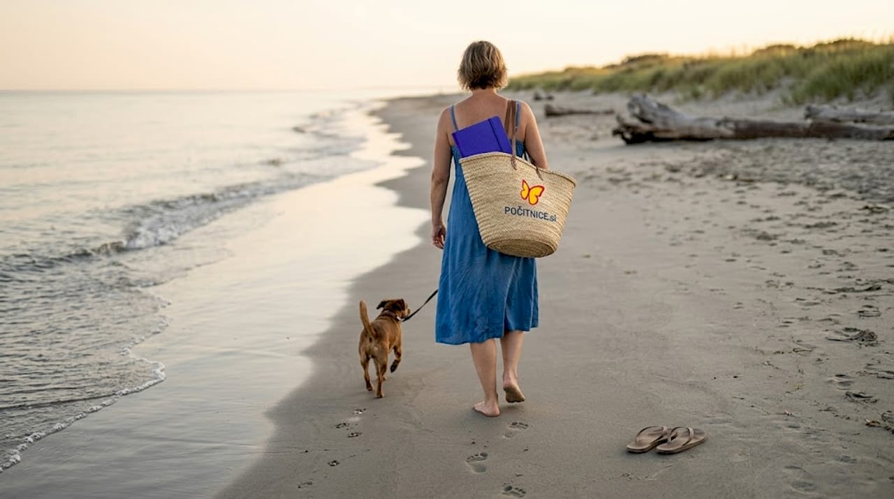 Po skoraj prazni plaži na Menorci se sprehajata ženska in njen pes.