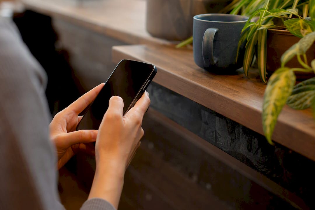 Eine Person steht unsicher an der Kasse und hält ihr Smartphone in der Hand.