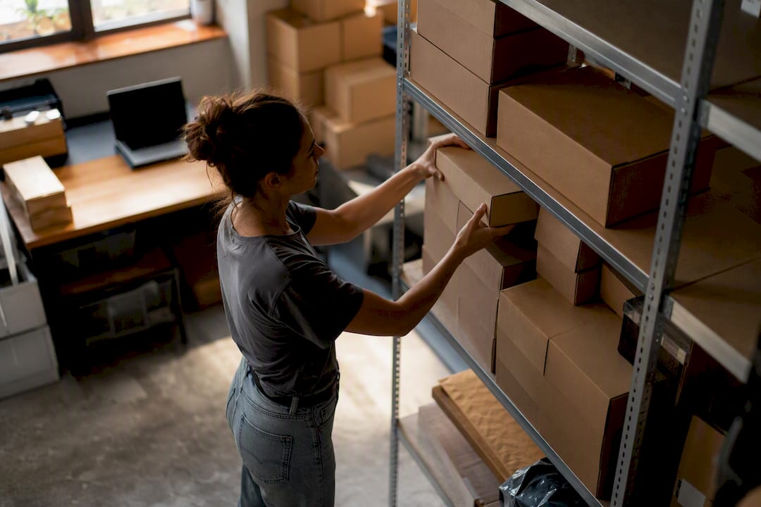 Hände, die Produktverpackungen in Lageregalen ordnen