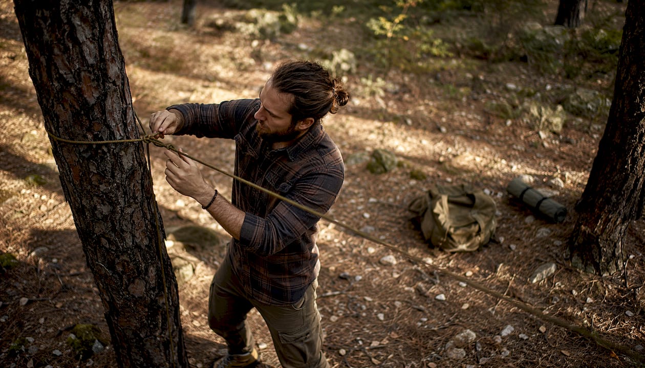 Person tying paracord ridgeline outdoors