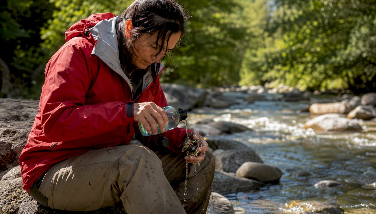 Hands rinsing fishing reel at riverbank