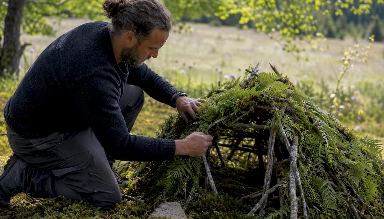 Hands layering debris on shelter frame