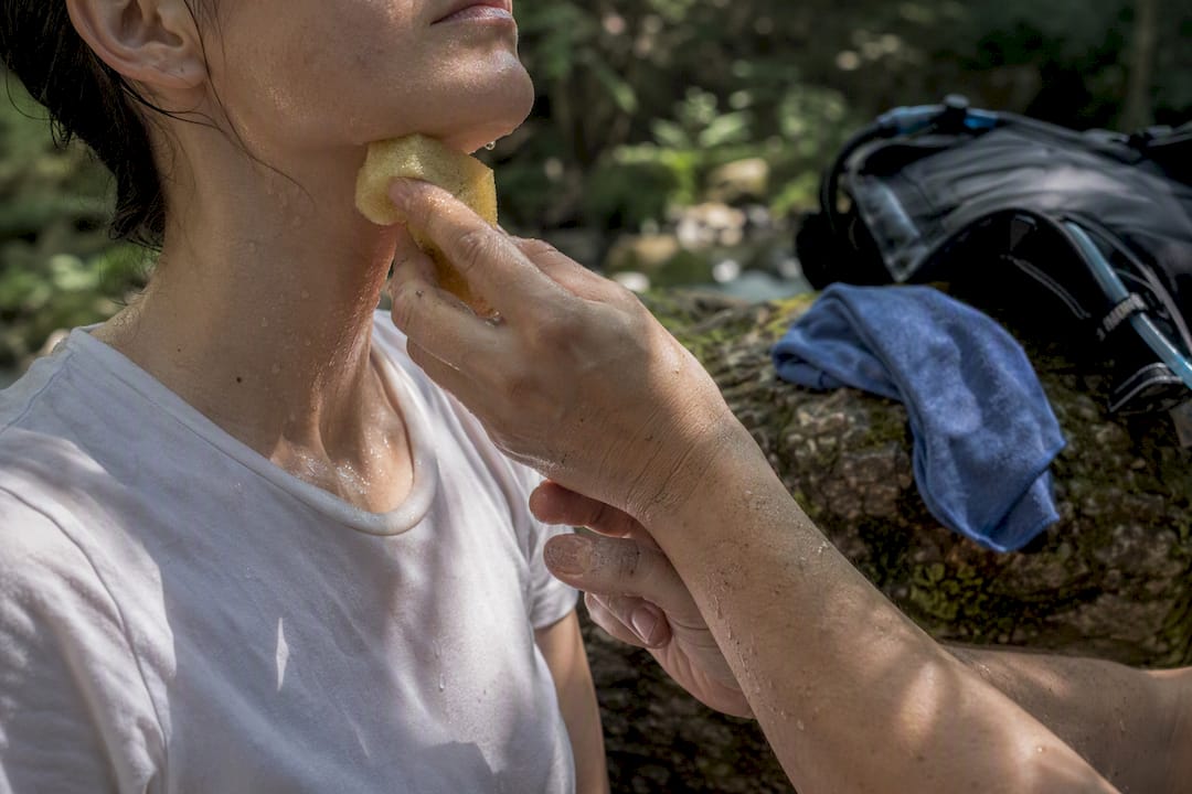 Hands applying wet sponge to neck and wrist