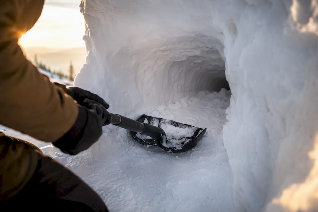 Hands digging snow cave entrance tunnel