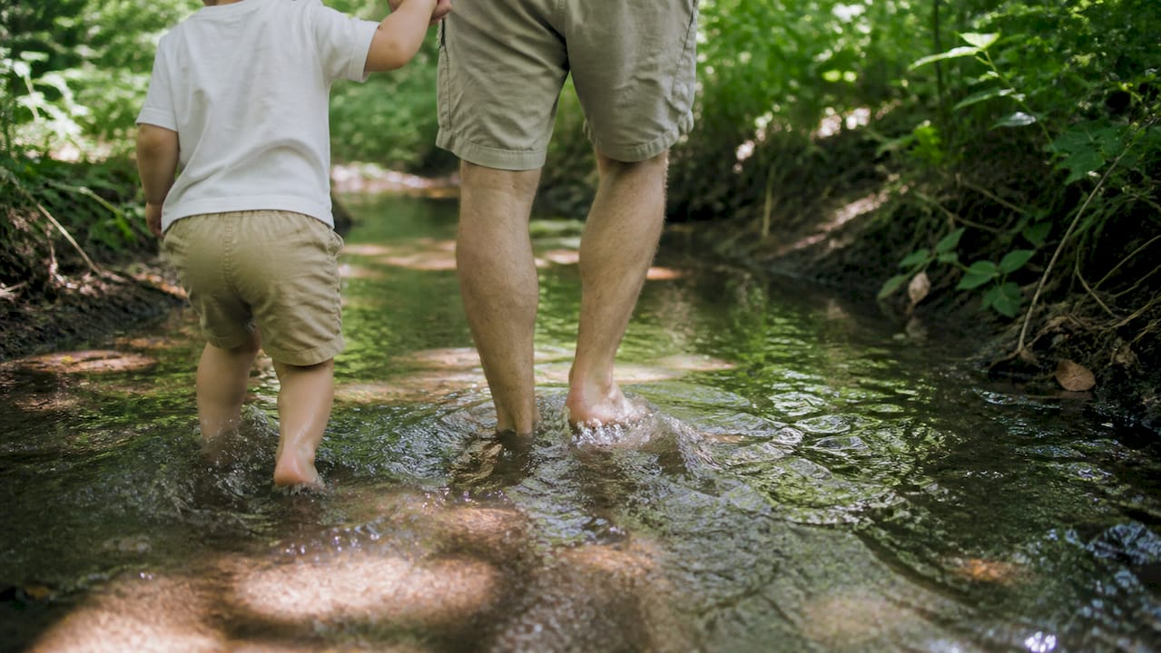 Adult holding child's hand crossing shallow flood water