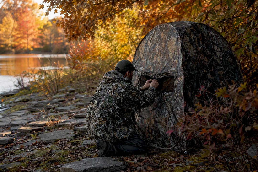 Photographer in camouflage poncho adjusting pop-up blind outdoors
