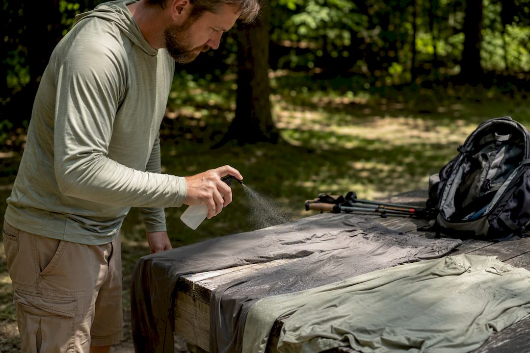 Hiker spraying permethrin on hiking clothes