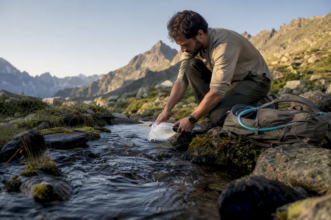 Hiker refilling water beside mountain stream