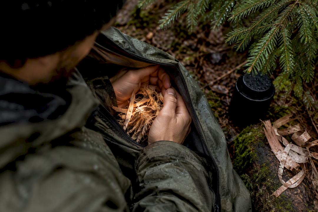 Camper warming dry tinder beneath conifers