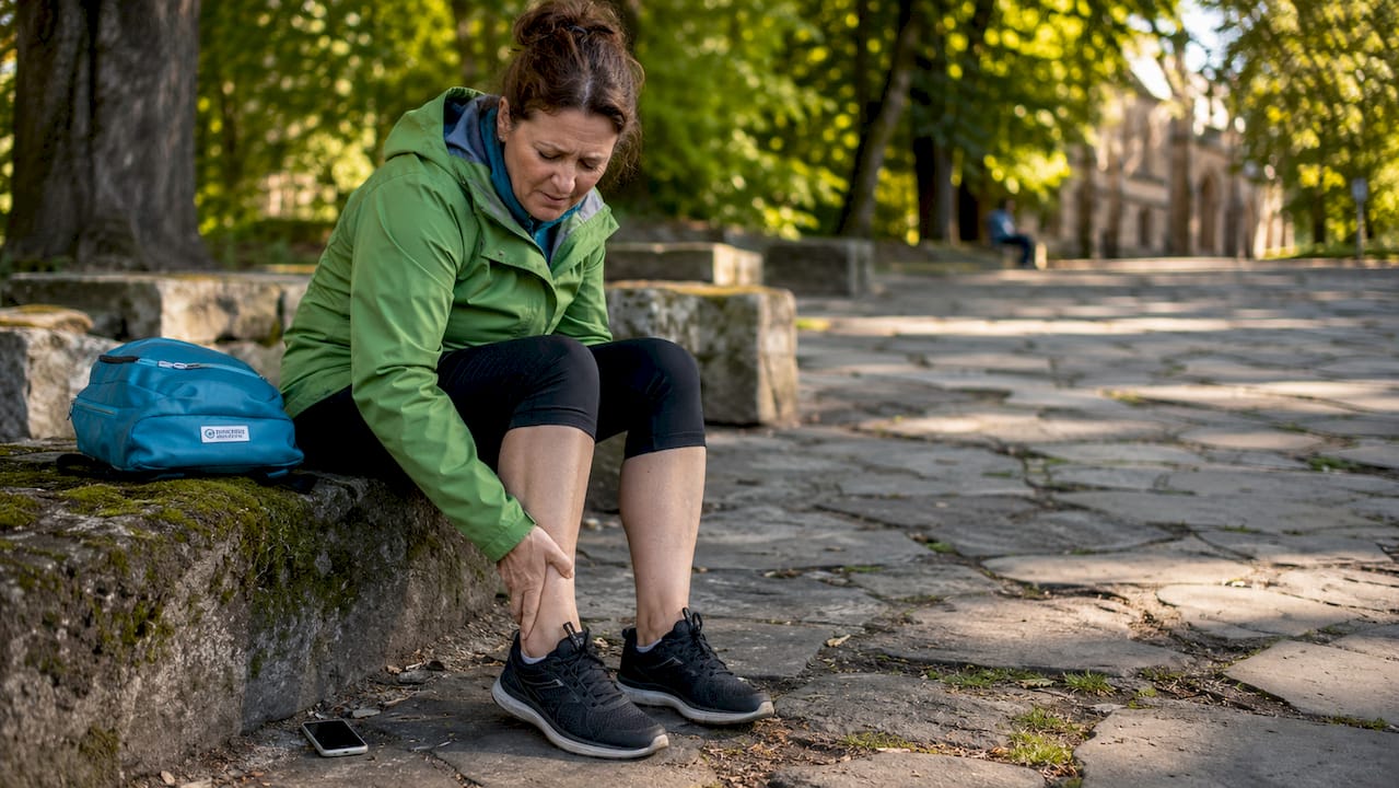 Woman seated near uneven pavement holding ankle