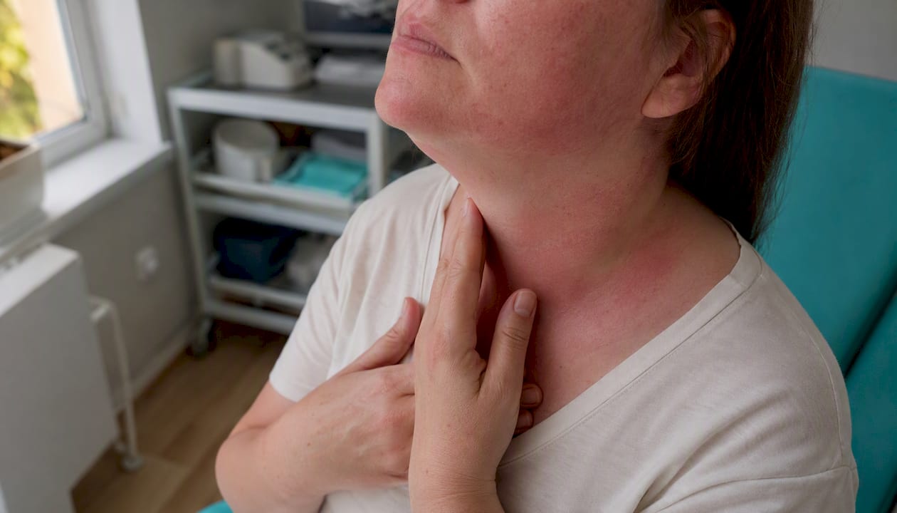 Femeie care își atinge zona gâtului, acolo unde tiroida este vizibil umflată