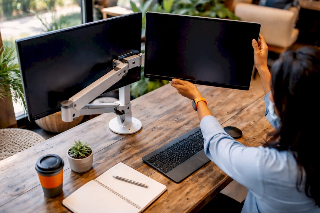 Hands adjusting dual monitors on different ergonomic supports