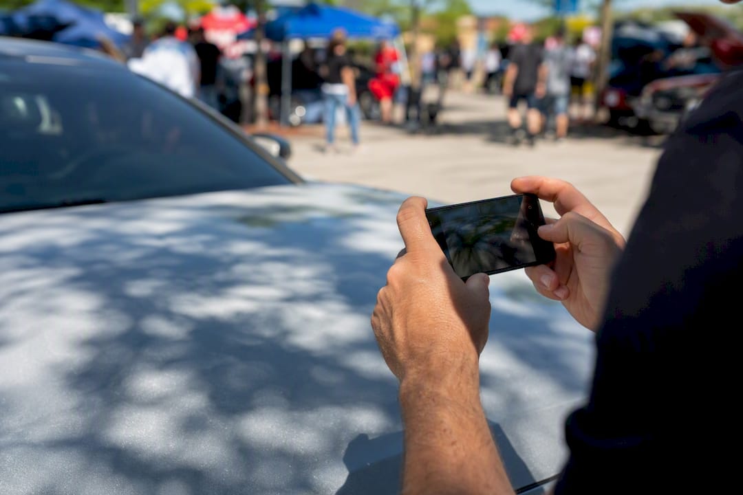 Hands photographing car hood with phone
