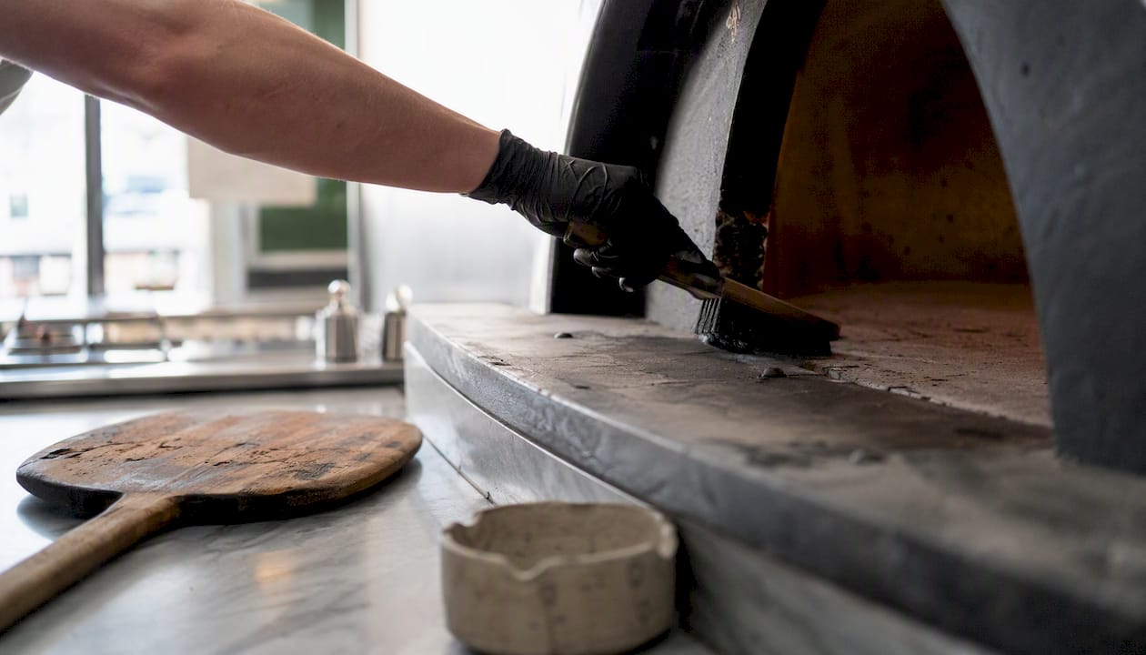 Pulizia manuale del piano cottura caldo di un forno pizza