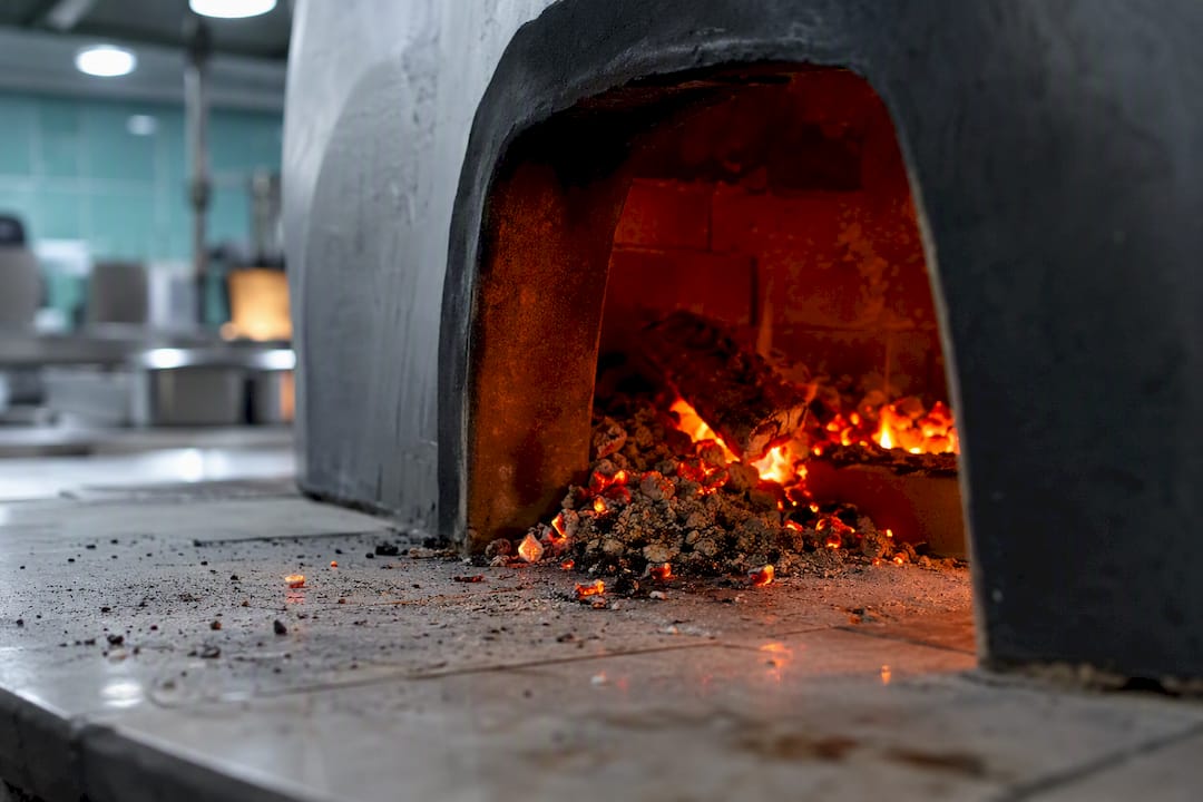 Brasas saliendo de la boca de un horno de pizza de leña