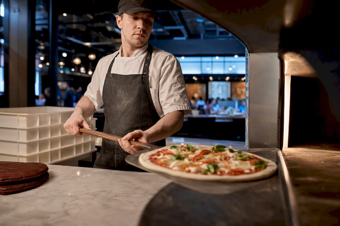 Chef cargando pizza en horno para food hall