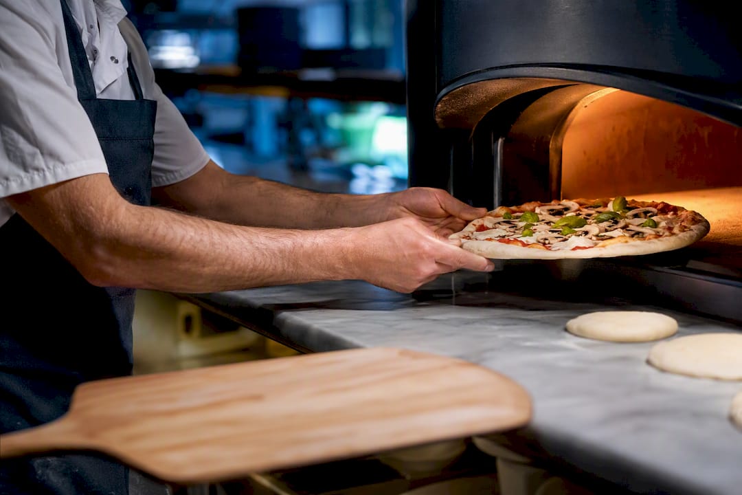 Koch belegt Pizza während des Stoßbetriebs