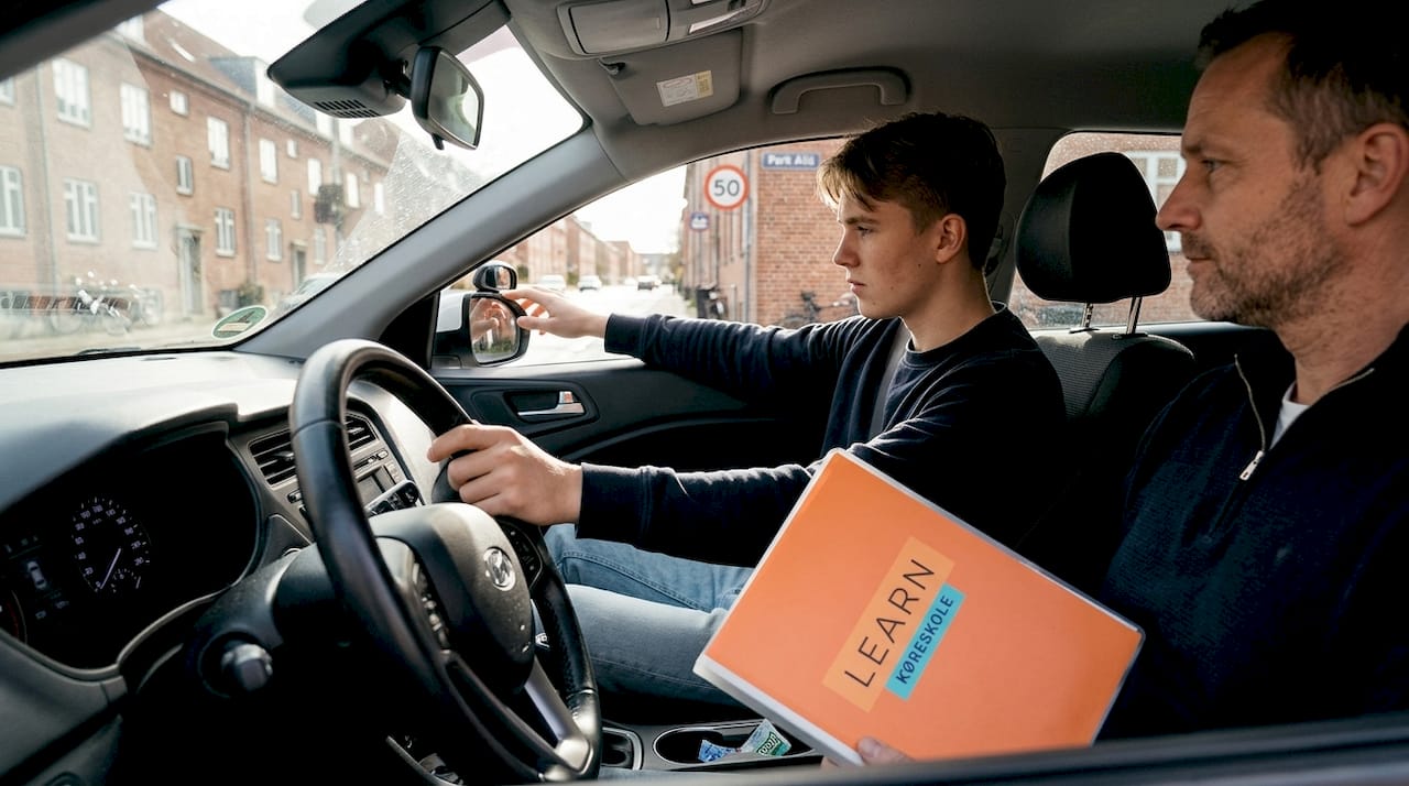 En køreelev retter på sidespejlet, mens han holder stille på en gade i Aarhus.