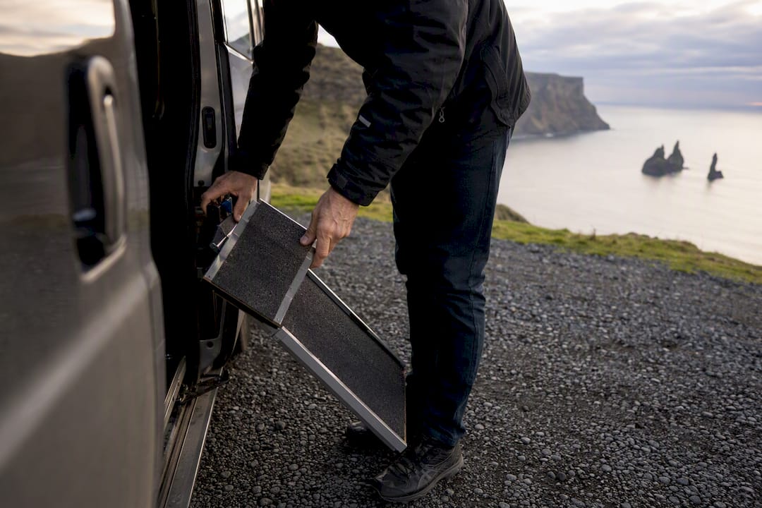 Hands deploying wheelchair ramp on transfer vehicle