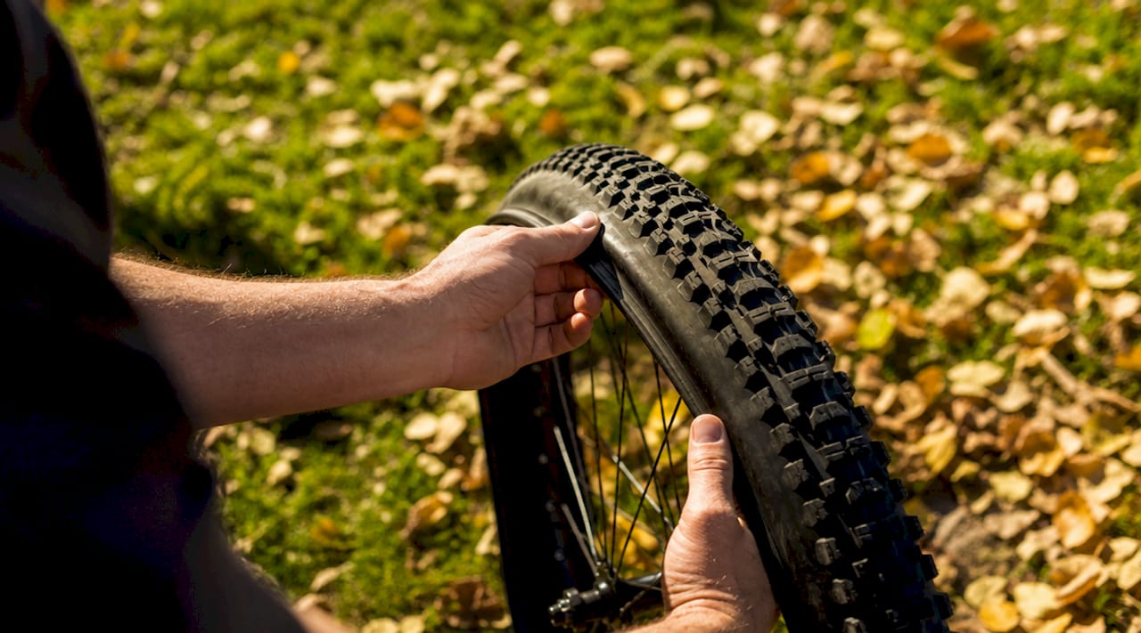 Buiten wordt een e-bikeband met grof profiel gemonteerd door vaardige handen.