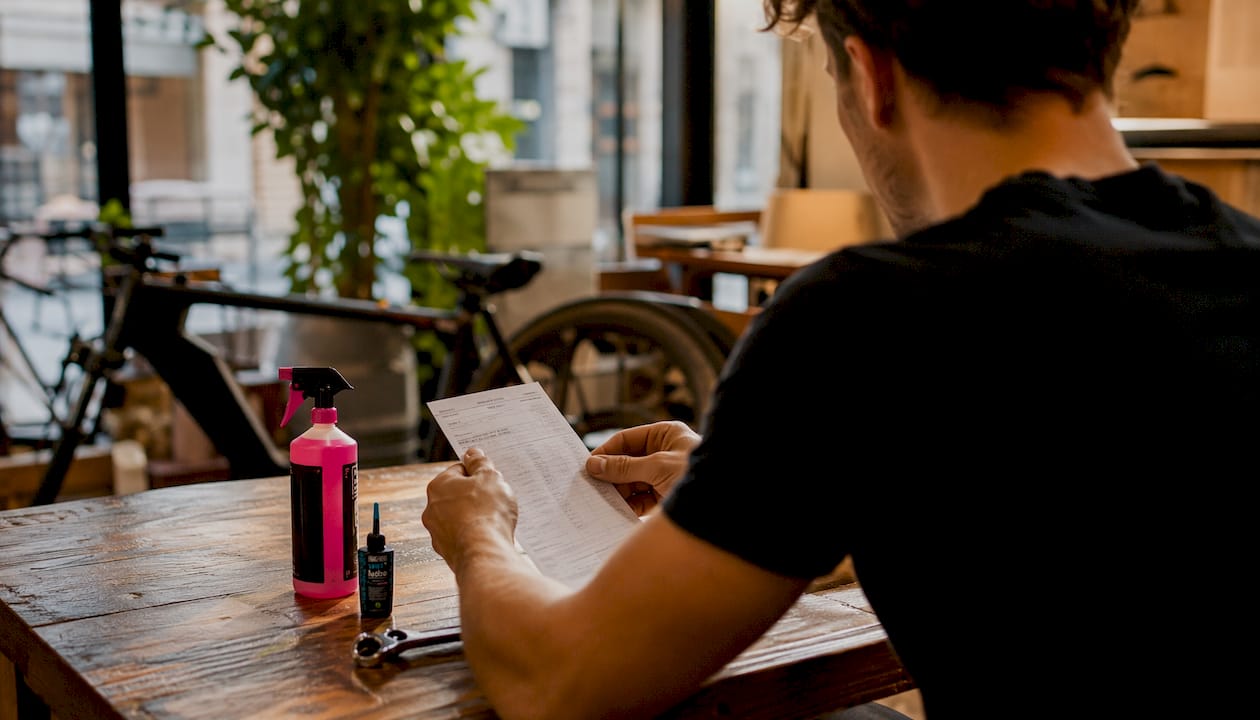 Iemand bladert door de fietsreparatiebon terwijl het gereedschap op de werkbank ligt.