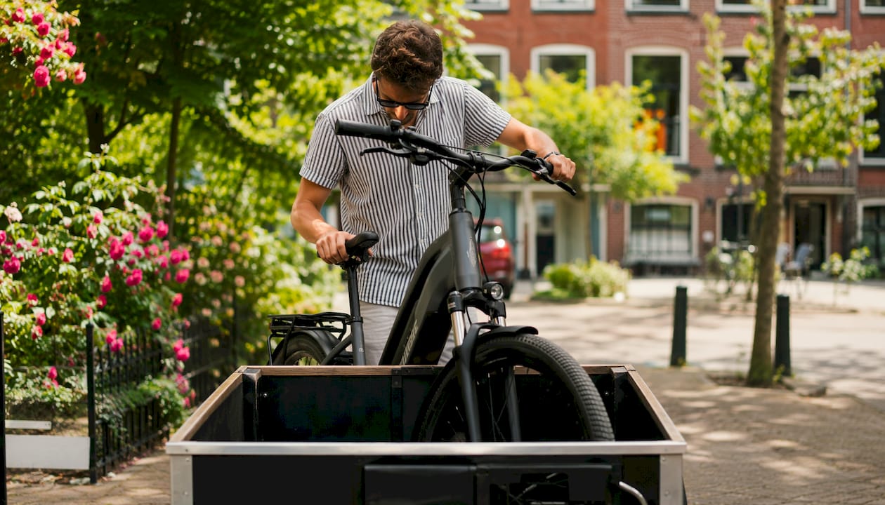 Een man zet zijn e-bike achterin de bakfiets.